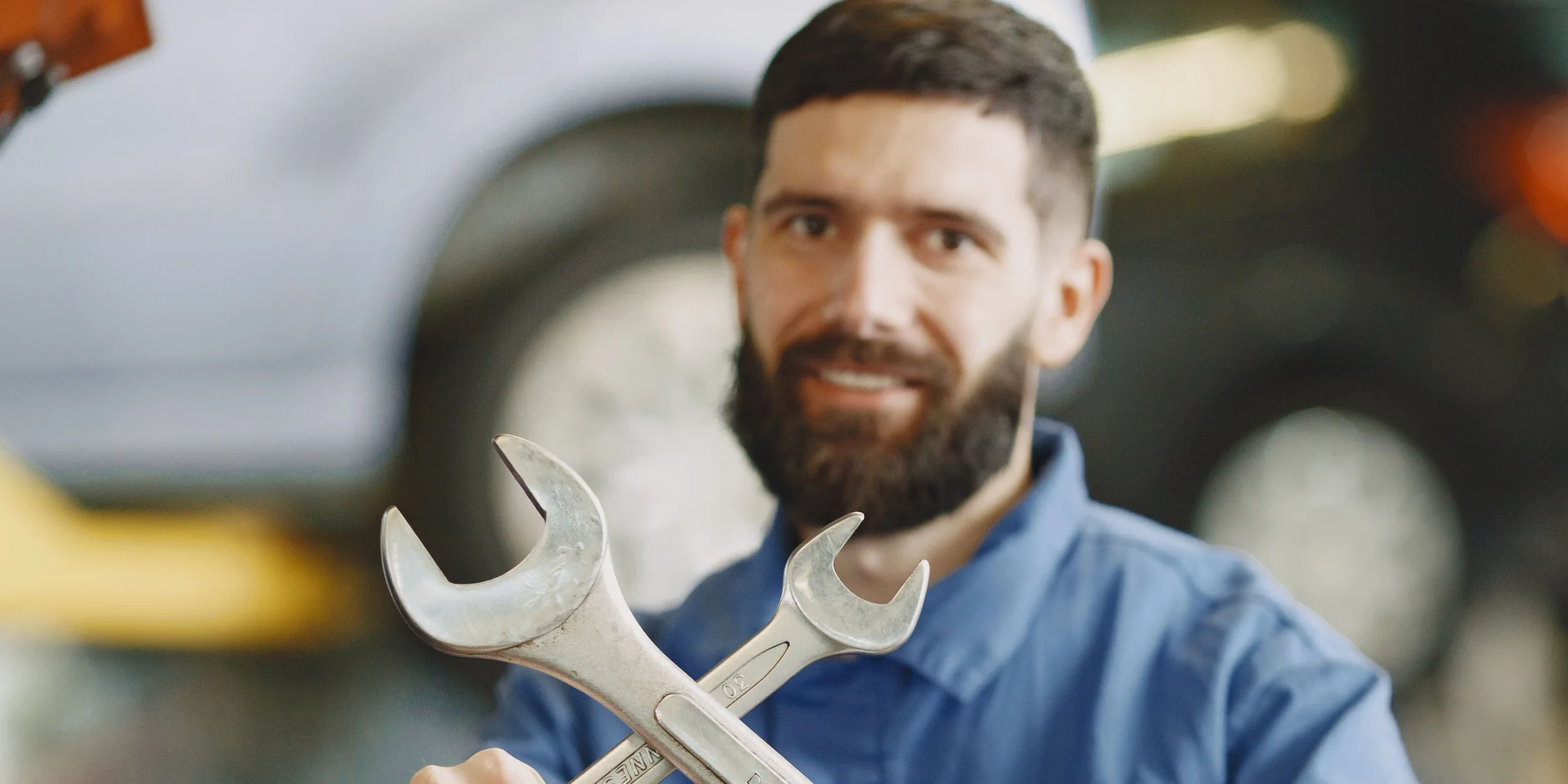 A technician in a workshop holding two open-ended wrenches