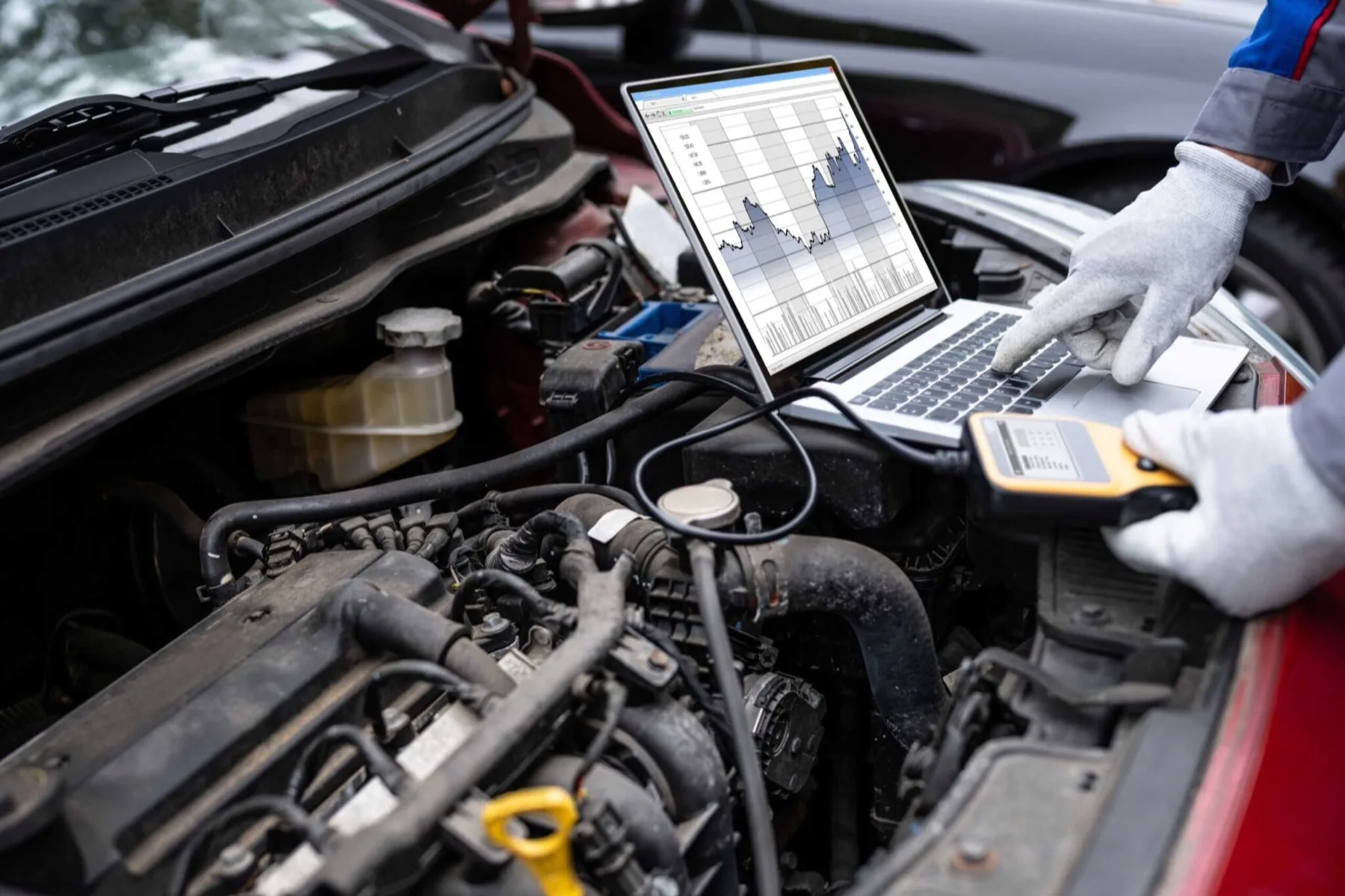 A technician running a laptop diagnostic scan in an open engine bay